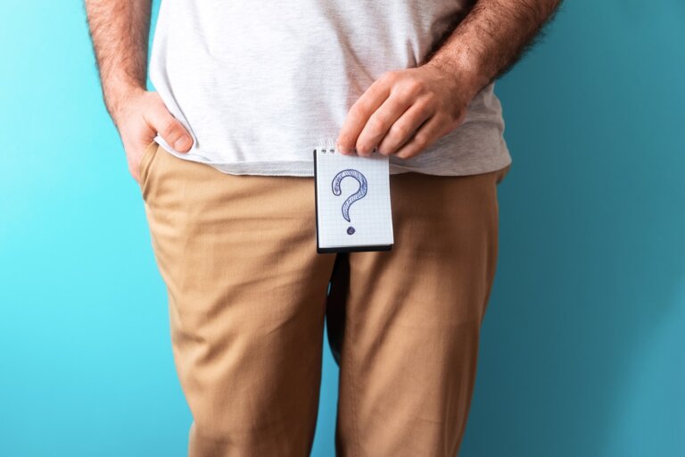 A man in beige jeans holds a notepad with question mark. Close up. Blue background